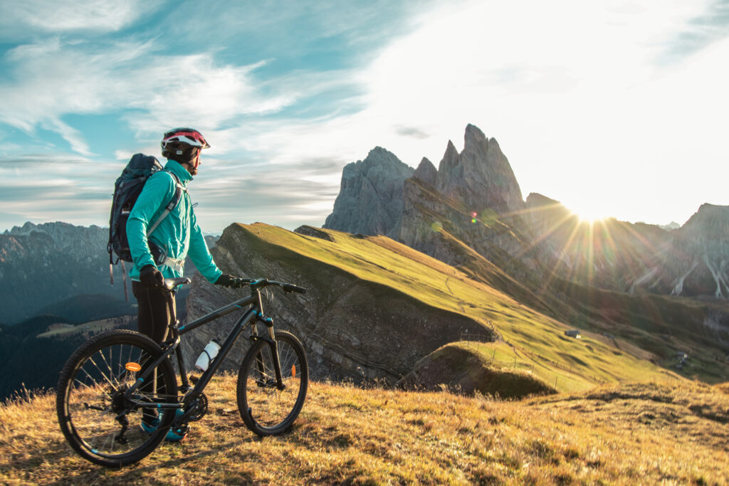 Young man with mountain bike cycling on Seceda mountain peak at sunrise in the Dolomites in Trentino