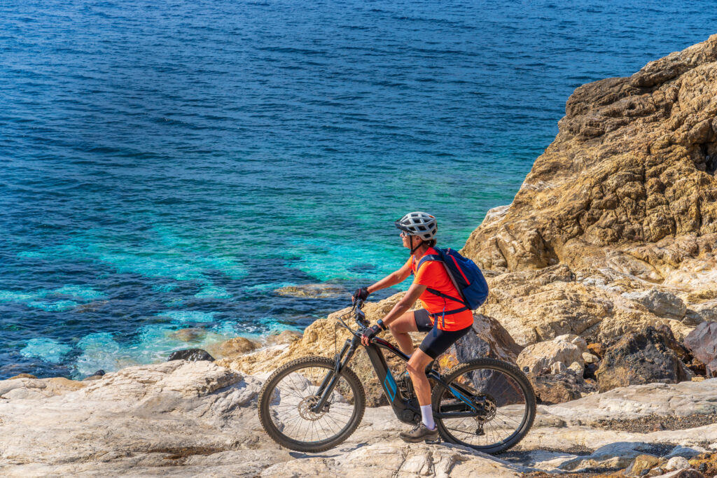 Woman riding her E-Bike at the coastline of mediterranean sea on the Island of Elba in the tuscan Archipelago in front of Porto Ferraio in Tuscany