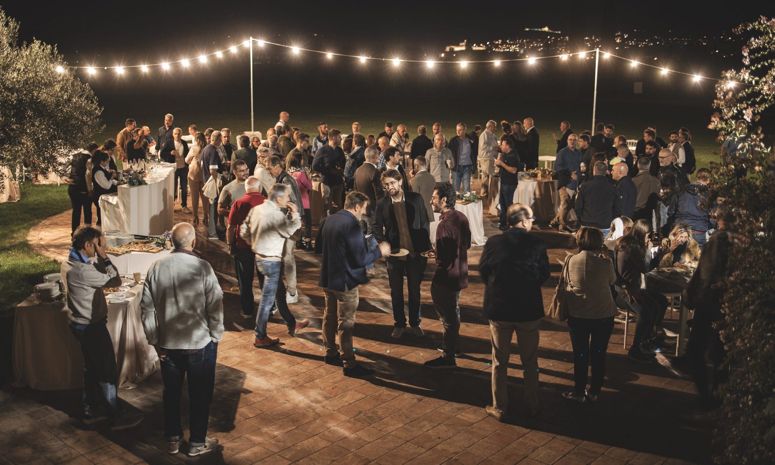 Group of people at a gathering, aperitif outside at night, lights.