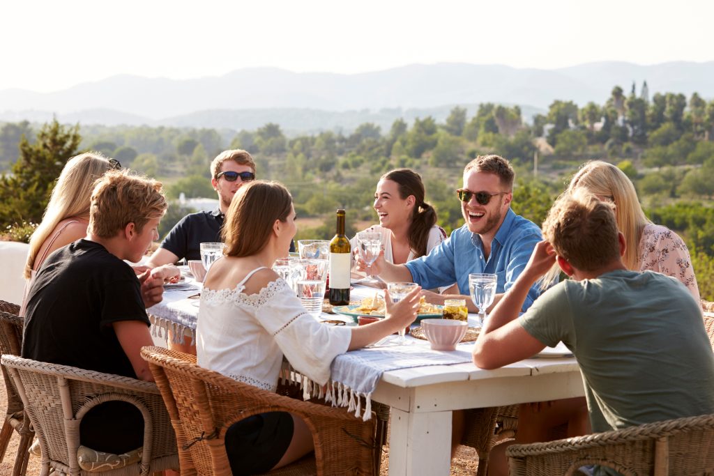 Gruppe von Leuten an Tisch draussen in der Natur mit Essen und Wein.