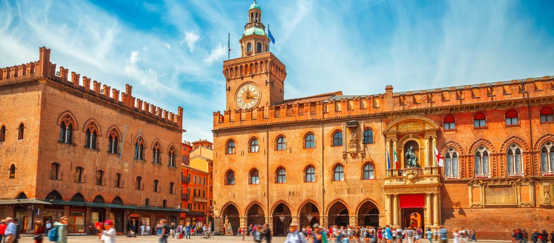 Italy Piazza Maggiore in Bologna old town tower of town hall with big clock and blue sky on background, antique buildings terracotta galleries