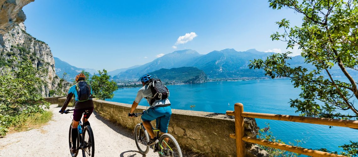 Radsport Frau und Mann fahren auf Fahrrädern bei Sonnenaufgang mit Blick auf Gardasee.